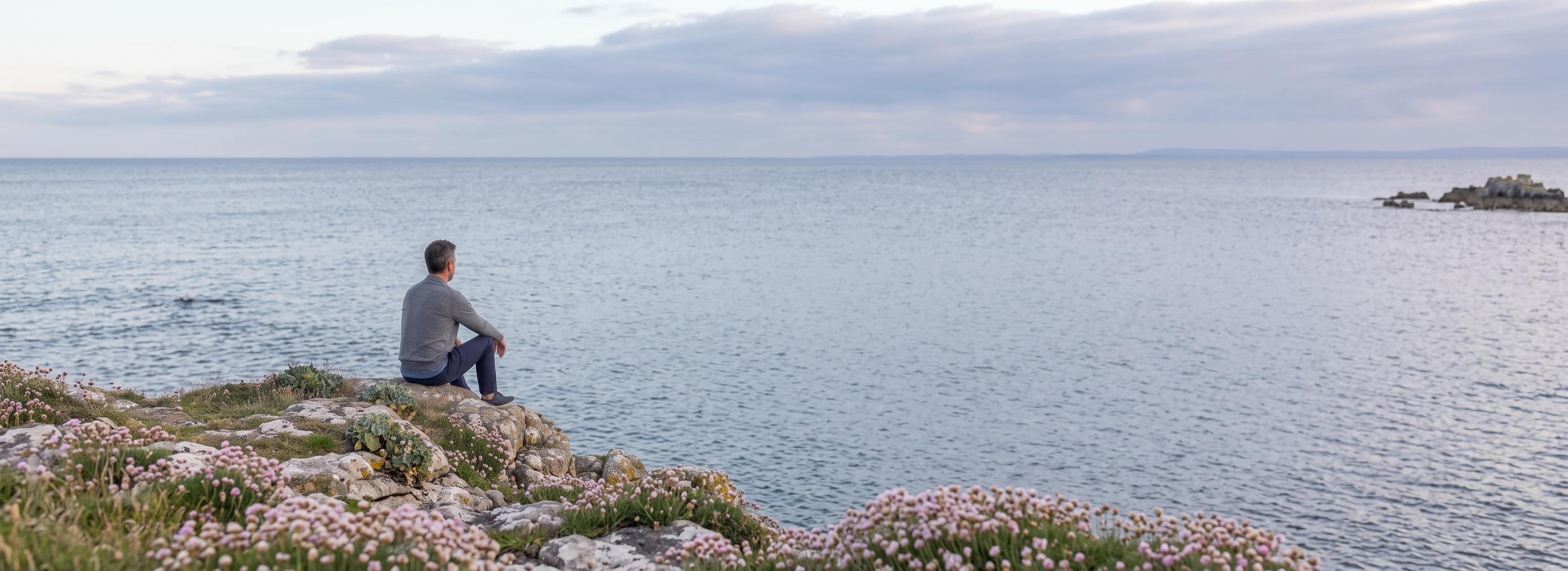 Hombre de espaldas contemplando un río al atardecer, rodeado de árboles y vegetación junto a la orilla.