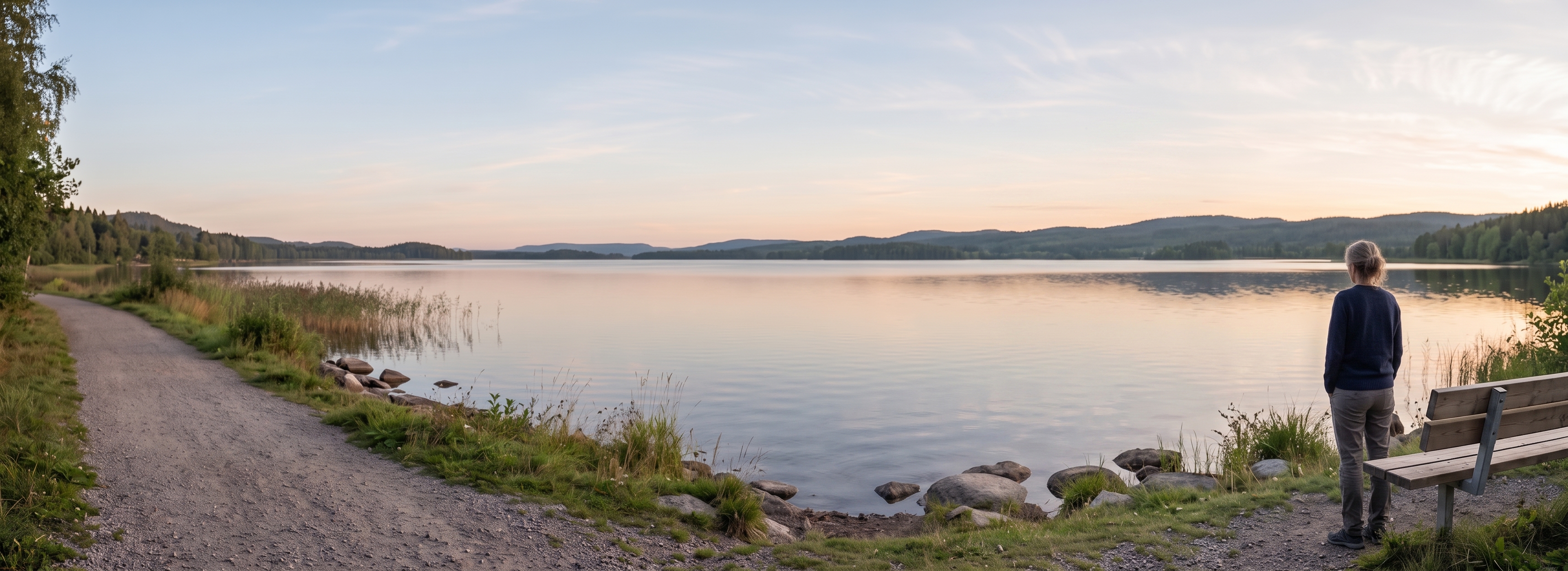 Mujer de espaldas junto a un lago, contemplando el paisaje al atardecer.