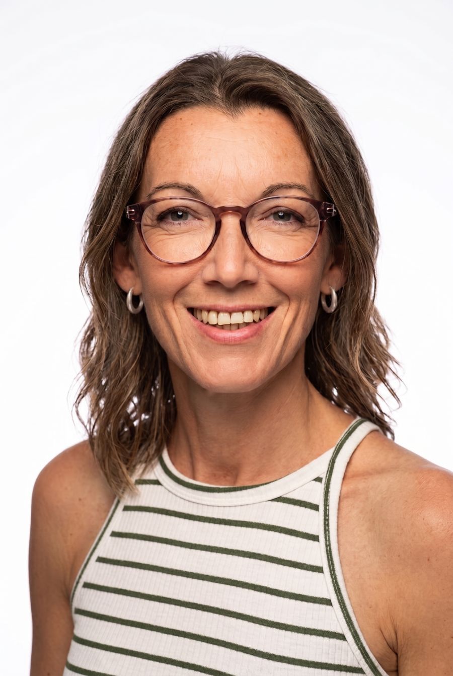 Retrato de una mujer sonriente con gafas y pendientes, de pelo castaño ondulado hasta los hombros, vestida con una camiseta de rayas verdes  sobre fondo blanco.